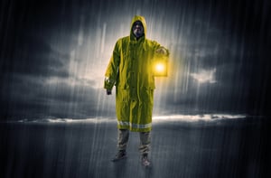 Raincoated man walking in storm with glowing lantern in his hand